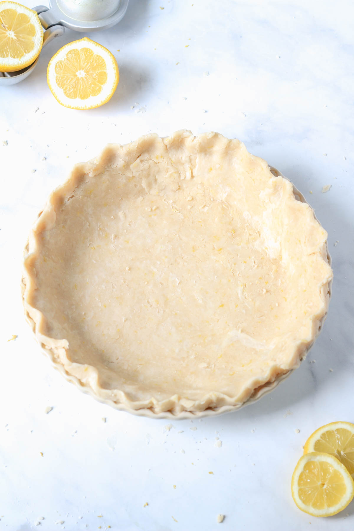 A pie pan with lemon pie dough before baking on a white counter.