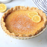 A simple, dairy-free lemon chess pie topped with lemon slices on a white counter.