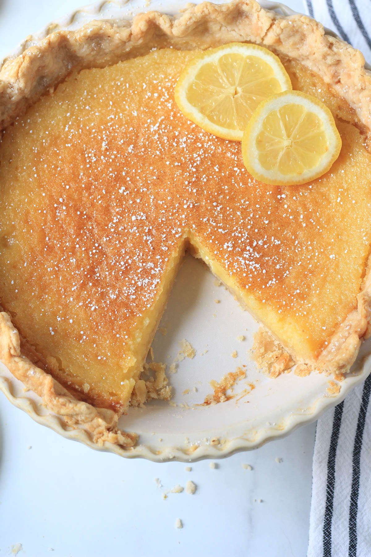 A top down picture of a lemon chess pie in a pie pan with a wedge taken out.