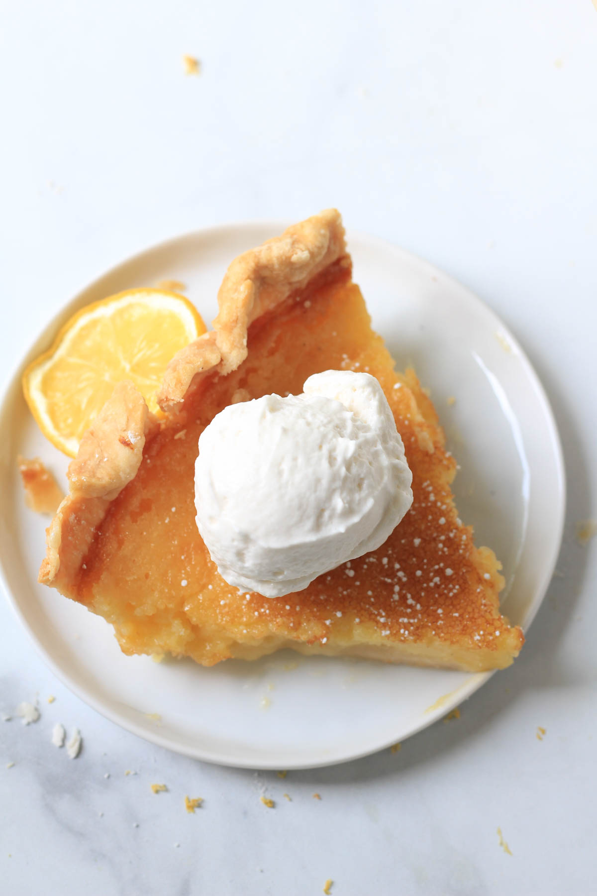 A slice of lemon chess pie on a white plate topped with dairy-free whipped topping.