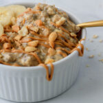 A close up of a gold spoon with a scoop of vegan vanilla peanut butter overnight oats in a white bowl.