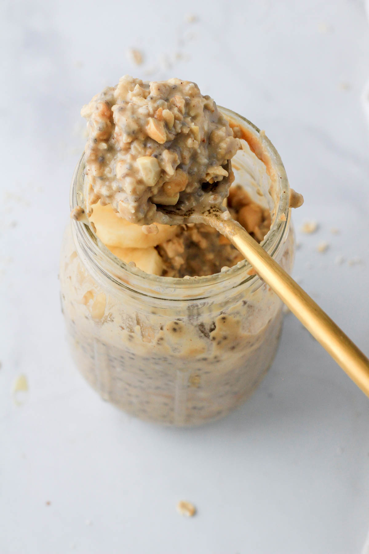 A glass mason jar with vegan vanilla peanut butter overnight oats on a gold spoon.