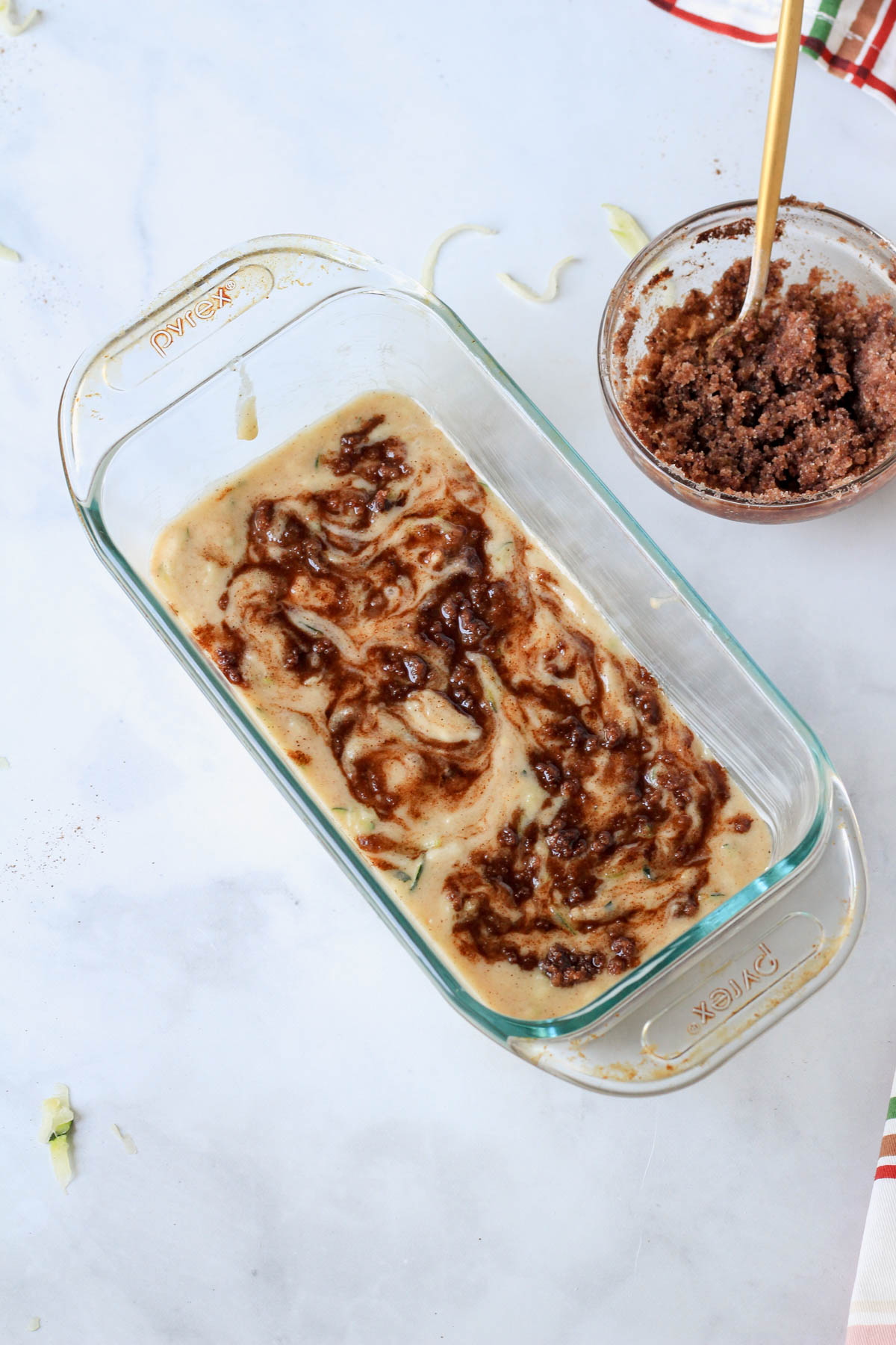 A glass loaf pan with zucchini bread batter topped with cinnamon swirl topping.