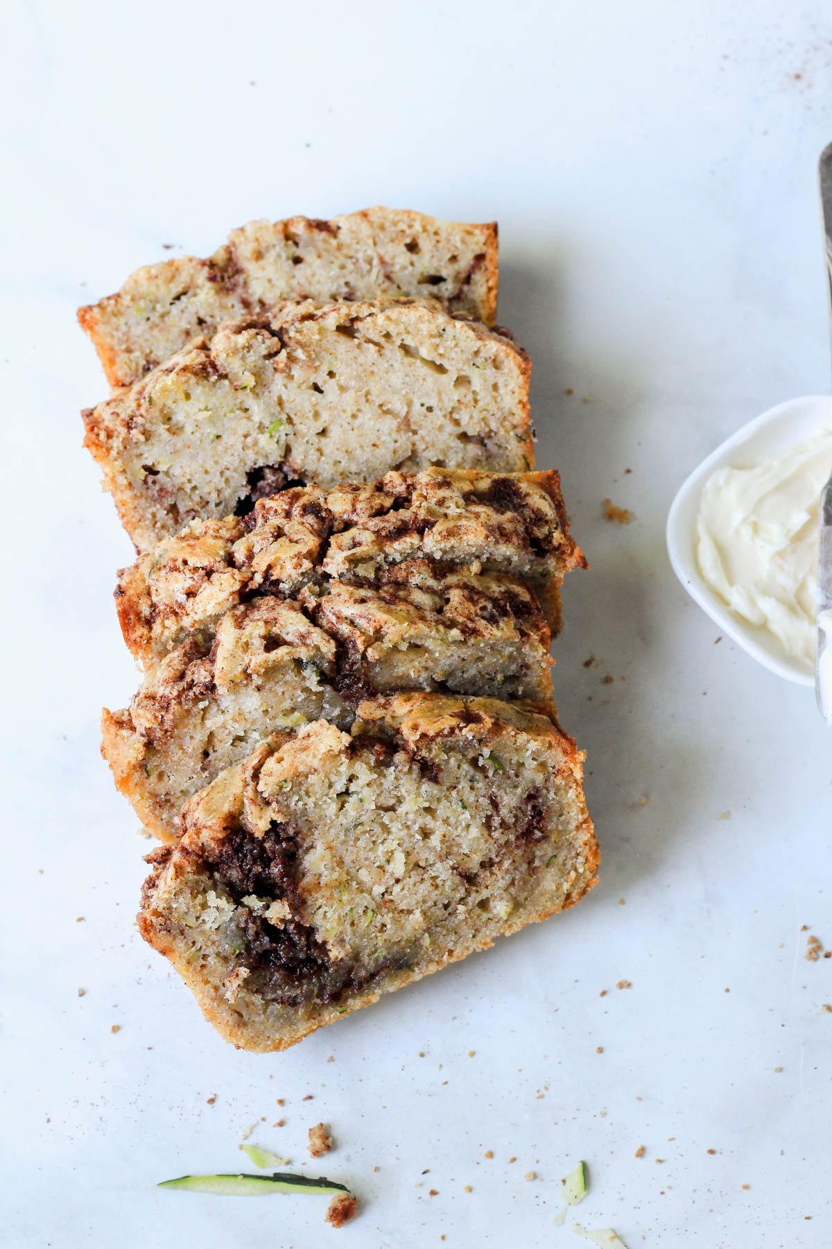 Five slices of dairy-free cinnamon swirl zucchini bread laying on a white counter.