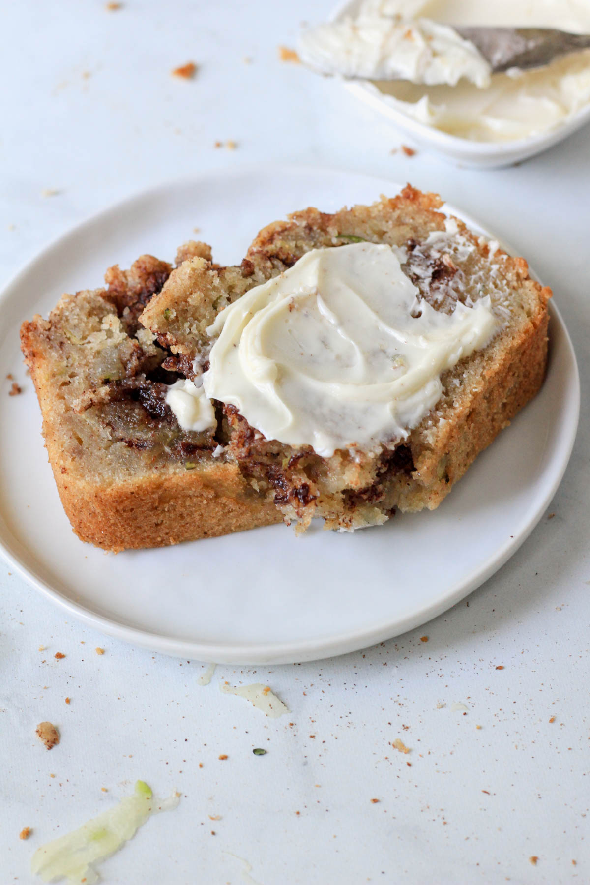 A small white plate with a slice of cinnamon swirl zucchini bread topped with dairy-free butter.