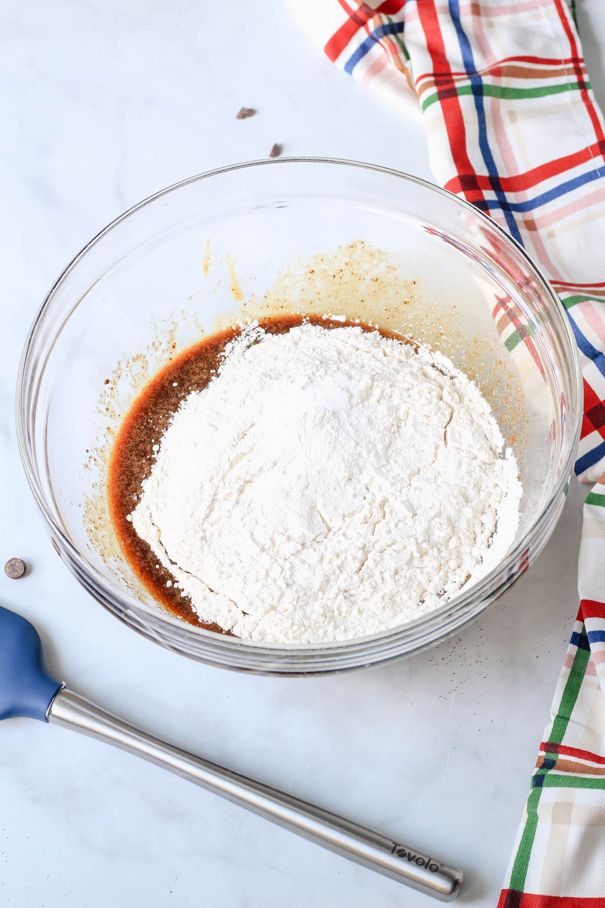 A glass bowl with the dry ingredients on top of the wet ingredients for the espresso chocolate chip cookie crust.