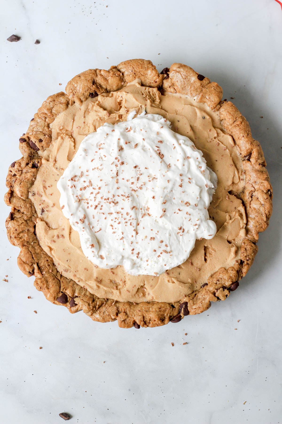 A dairy-free ice cream pie topped with dairy-free whipped cream on a white counter.