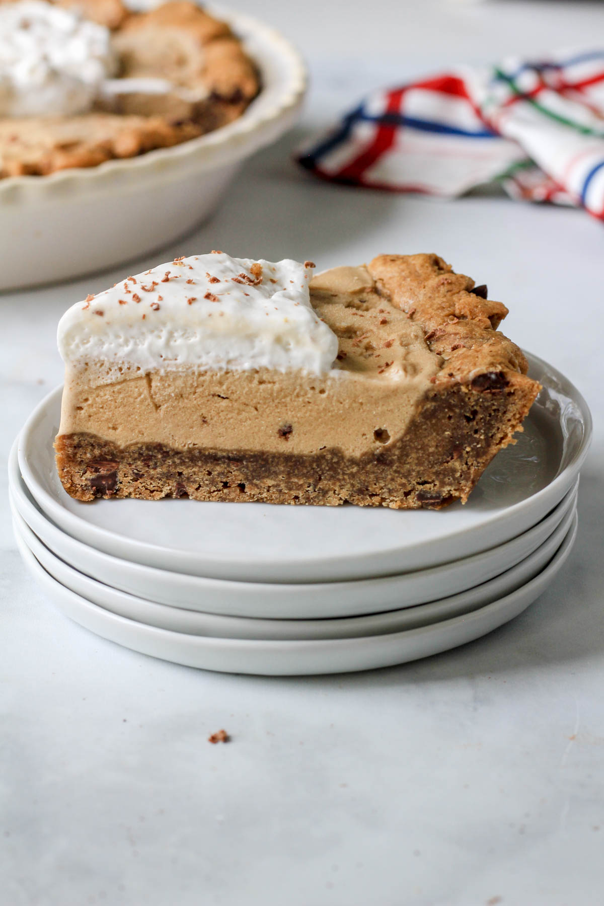 A stack of white plates with a slice of coffee chip ice cream pie on top.
