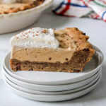 A stack of white plates with a slice of coffee chip ice cream pie topped with whipped cream.
