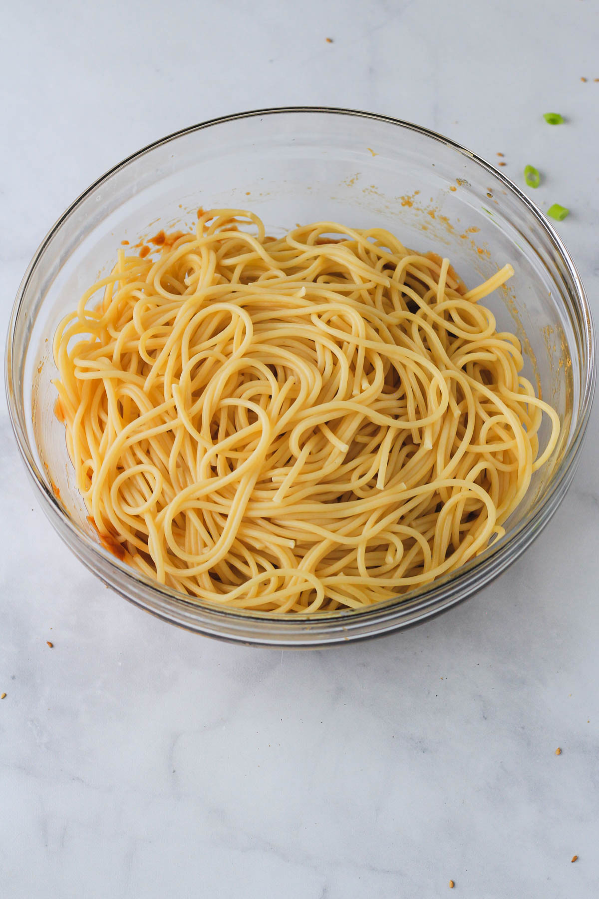 A glass bowl with peanut sauce on bottom and cooked spaghetti noodles on top.