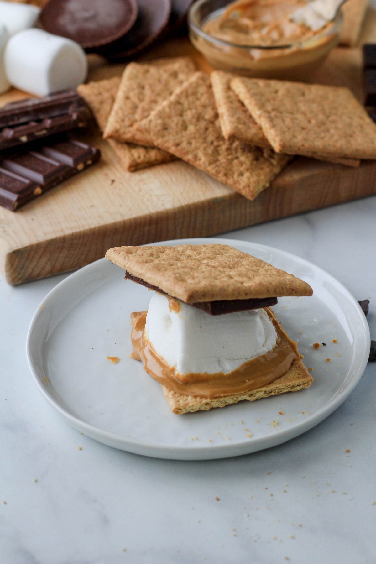 A white plate with a dairy-free s'more slathered with peanut butter.