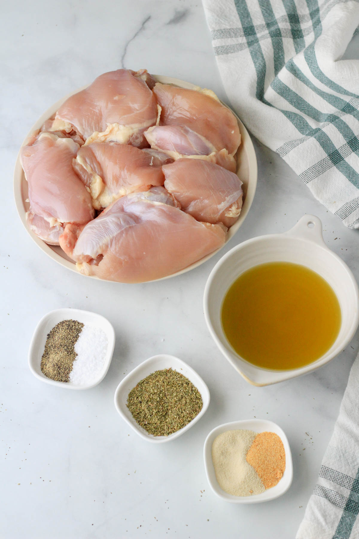 Ingredients for Italian Marinated Grilled chicken thighs on a white counter with a green and white dish towel.