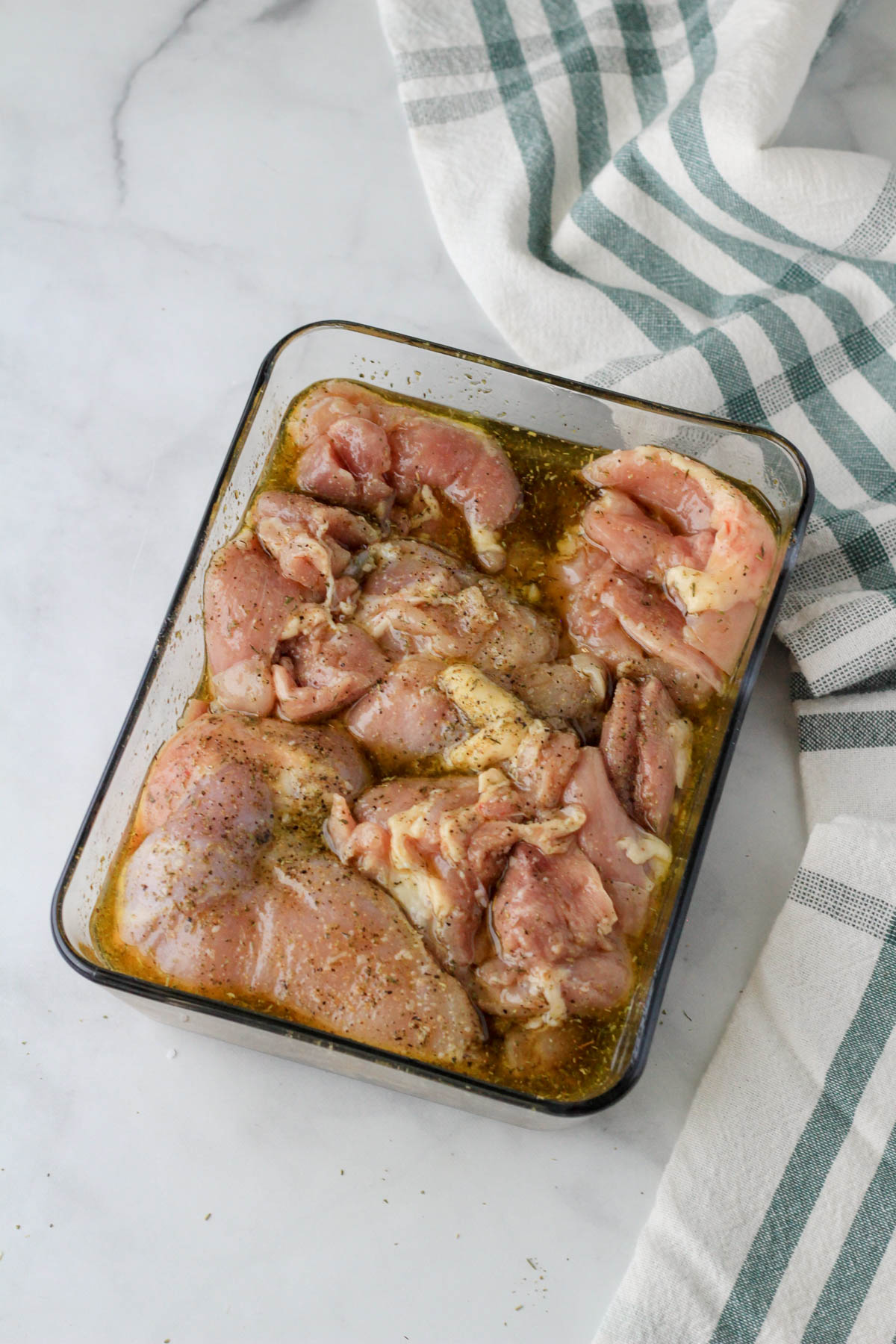 A glass Pyrex with chicken thighs coated in Italian marinade.