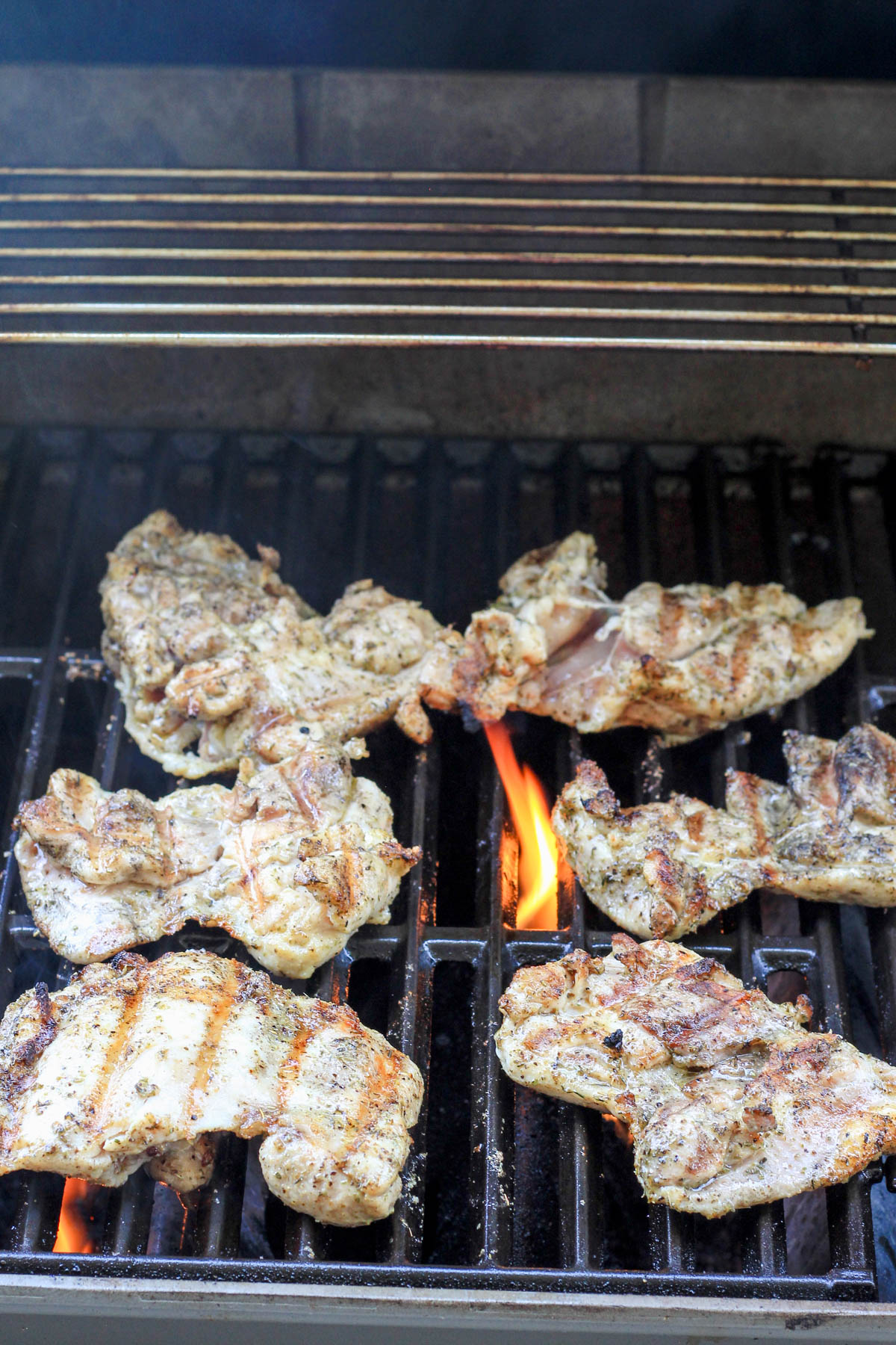 A grill with Italian marinated chicken thighs cooking.