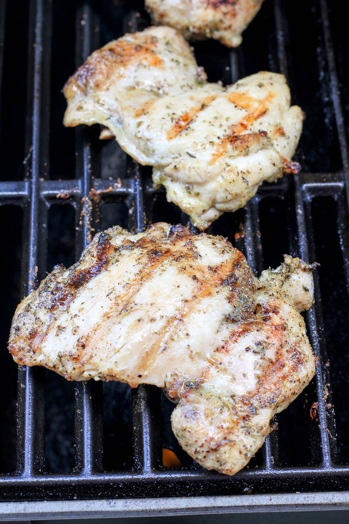 Two Italian marinated chicken thighs cooking on a grill.