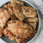 Italian marinated grilled chicken thighs on a green and white plate.