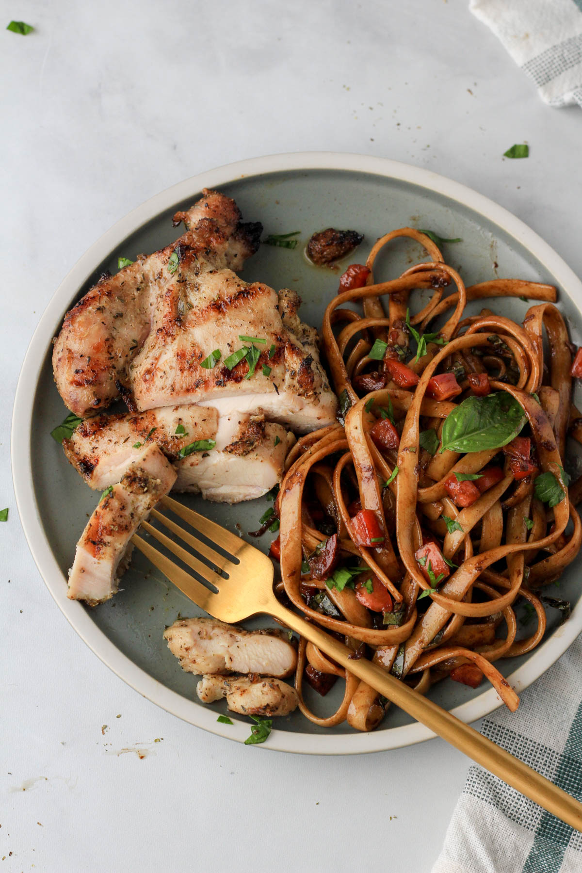 A gold fork with a slice of Italian marinated grilled chicken on a green plate with pasta.