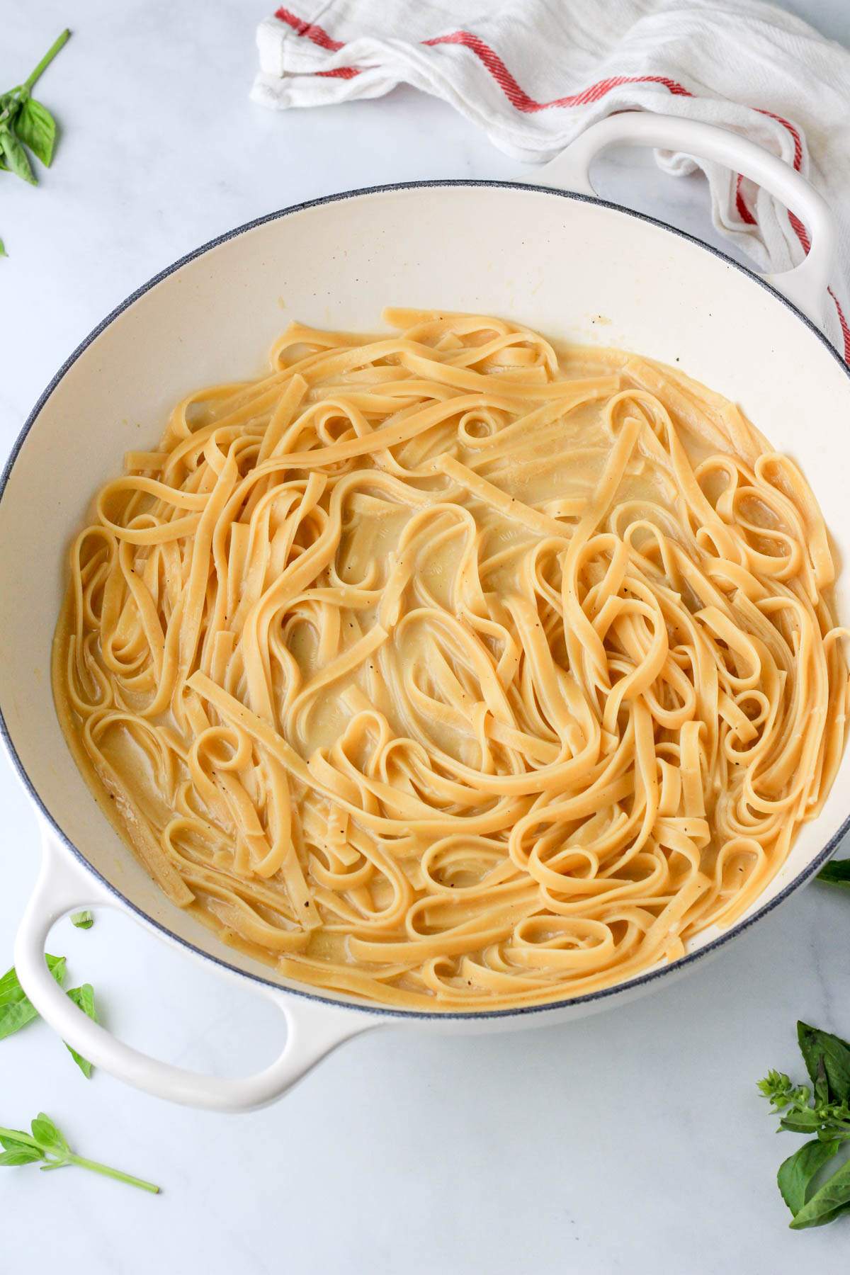 A pot of cooked pasta with garlic sauce on a white counter.