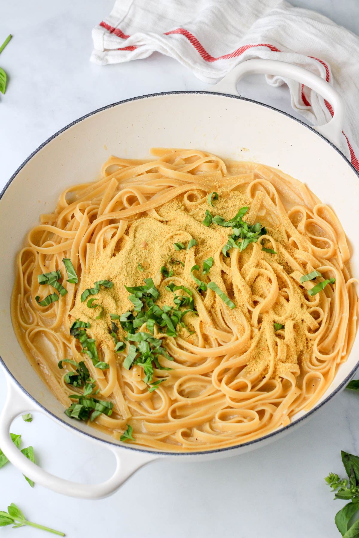 One pot vegan garlic pasta topped with nutritional yeast and basil before mixing together.