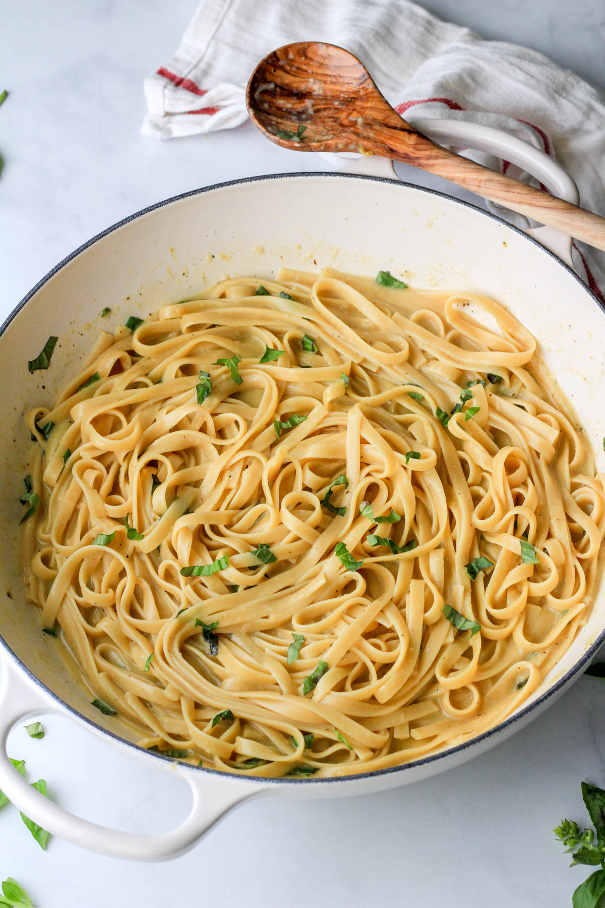 Vegan one pot garlic pasta in a white pan with a wooden spoon on the top right handle.