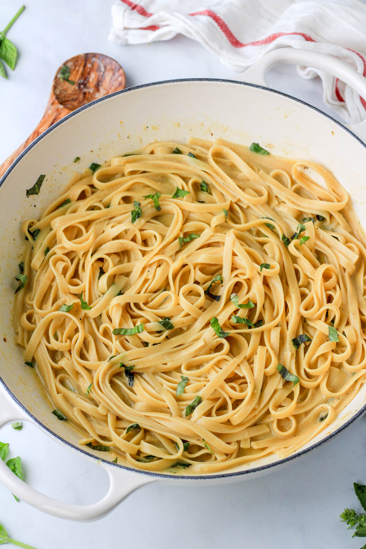 Vegan one pot garlic pasta on a white counter with a wooden spoon in the back left corner.