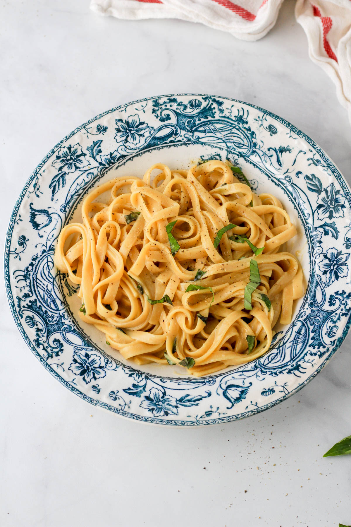 A white and blue bowl with a serving of one pot garlic vegan pasta topped with basil, salt, and pepper.
