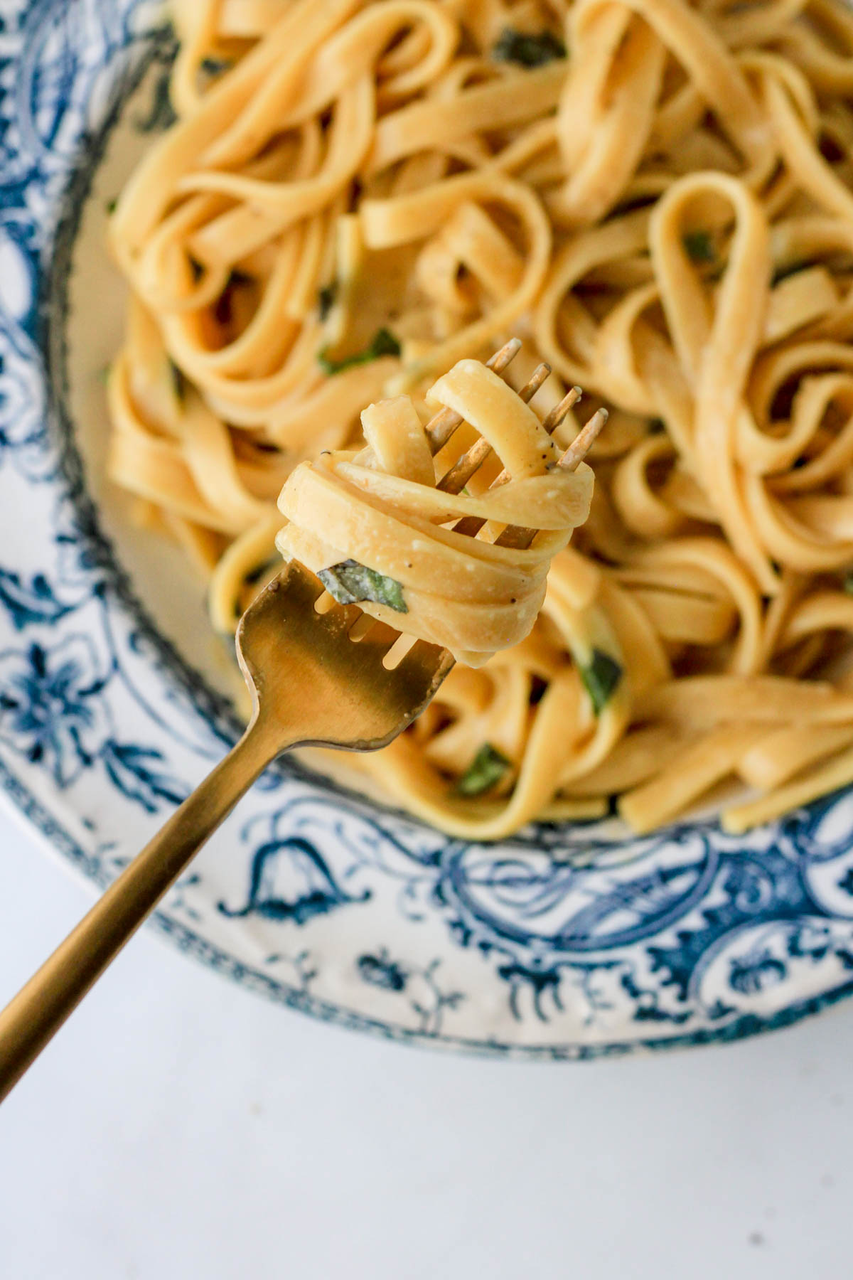 A gold fork with vegan garlic one pot pasta over a blue and white bowl.