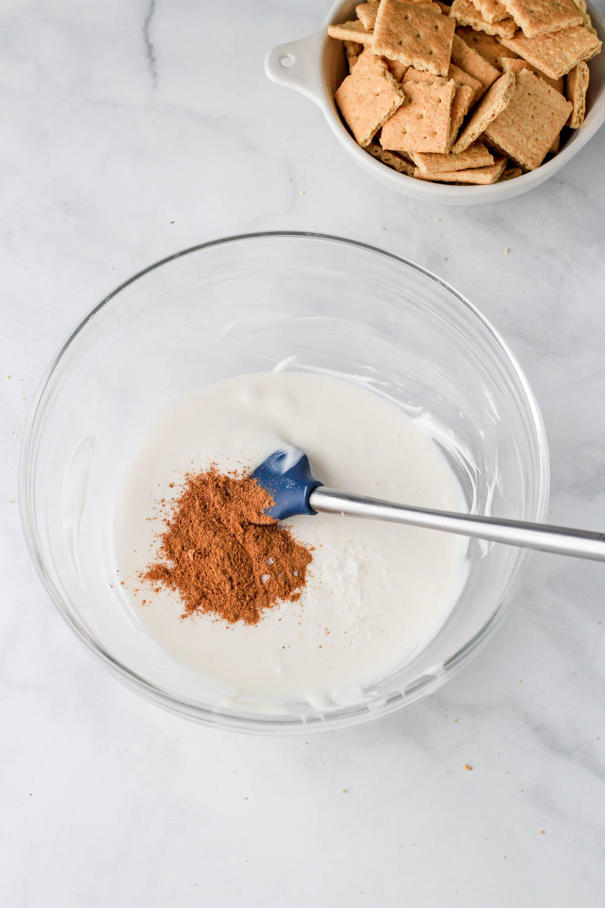A large glass bowl with melted white chocolate, pumpkin pie spice, and salt before stirring together.