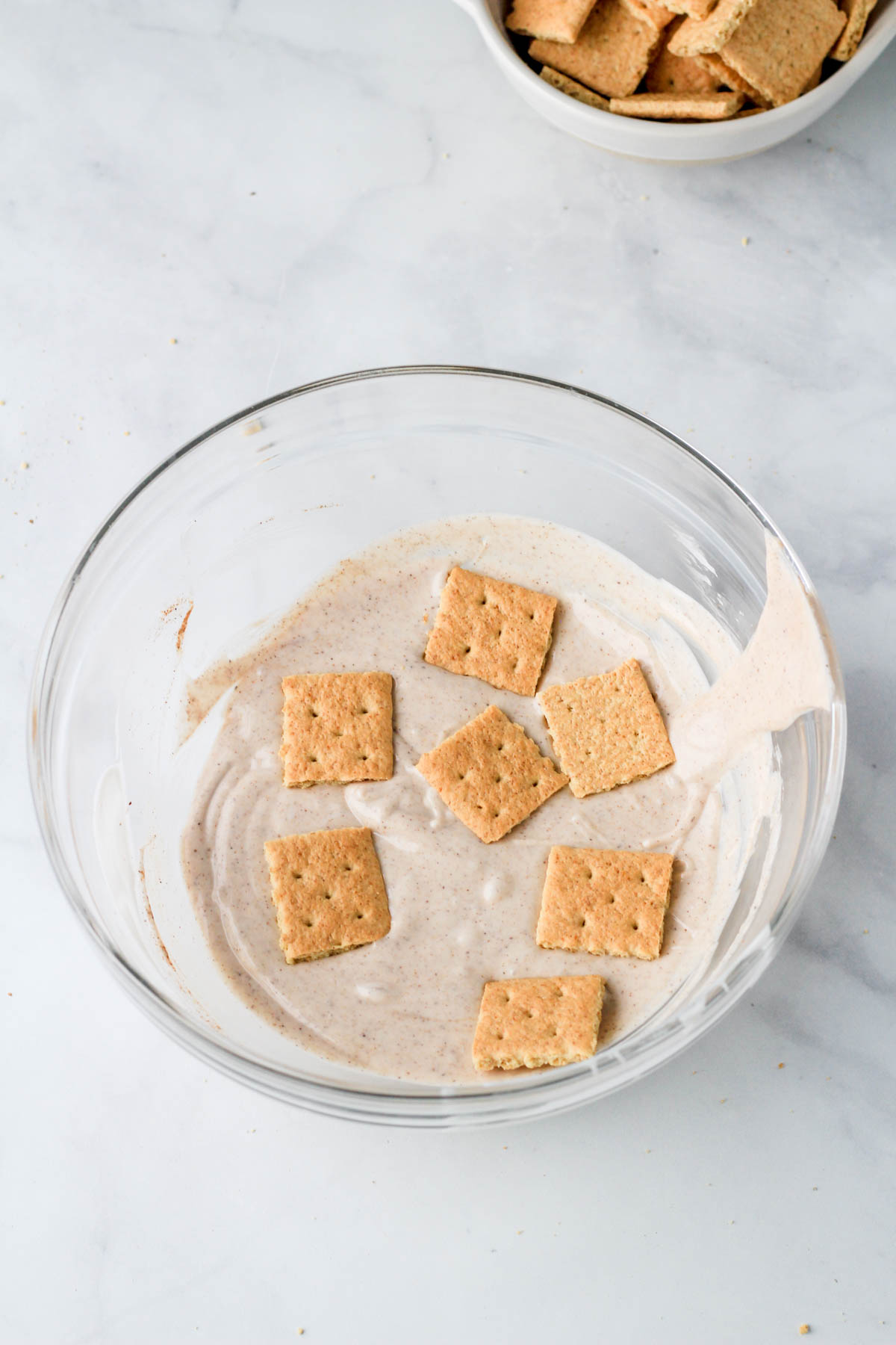 A large glass bowl with graham crackers before fully coating with the pumpkin pie spice white chocolate.