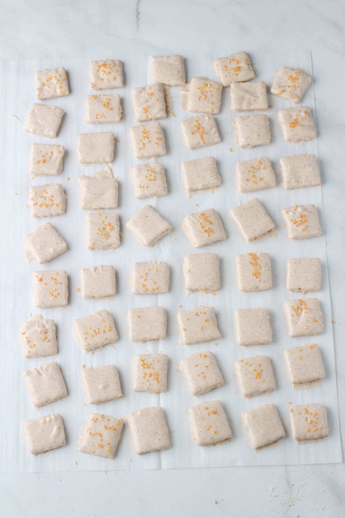 A white parchment paper covered in dairy-free pumpkin pie spice white chocolate dipped graham crackers after setting.