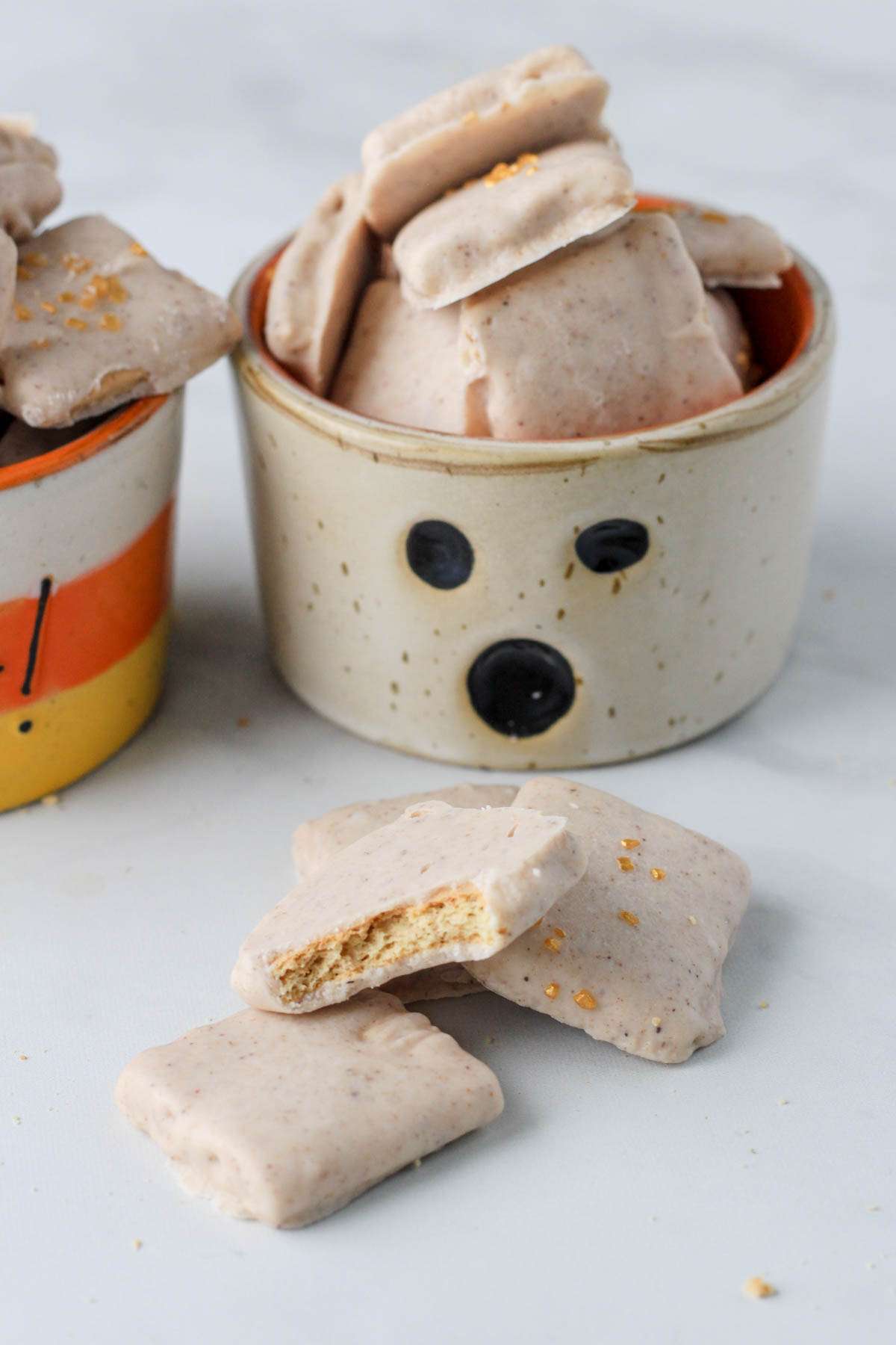 A small white ghost decorated bowl filled with dairy-free pumpkin spice white chocolate dipped graham crackers.
