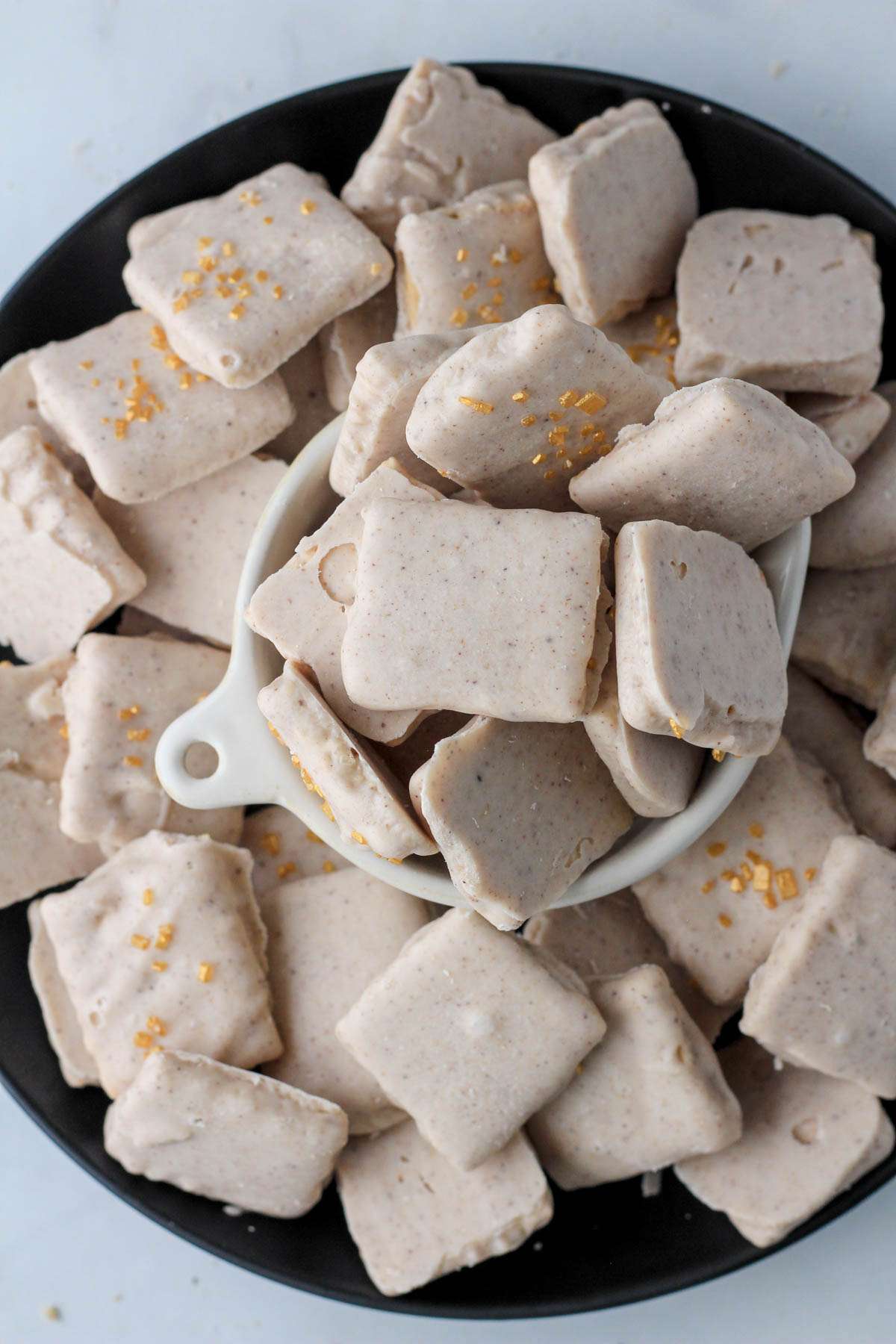 A black plate with a small bowl in the middle filled with white chocolate pumpkin spice graham crackers.