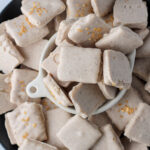 A small white bowl on a black plate surrounded by dairy-free white chocolate dipped pumpkin spice graham crackers.