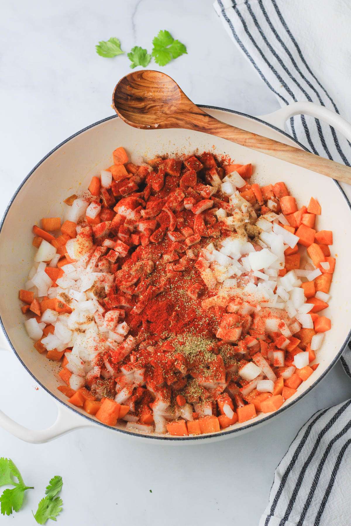A white skillet with cooked sweet potato, seasoning, raw turkey, and onion before cooking.
