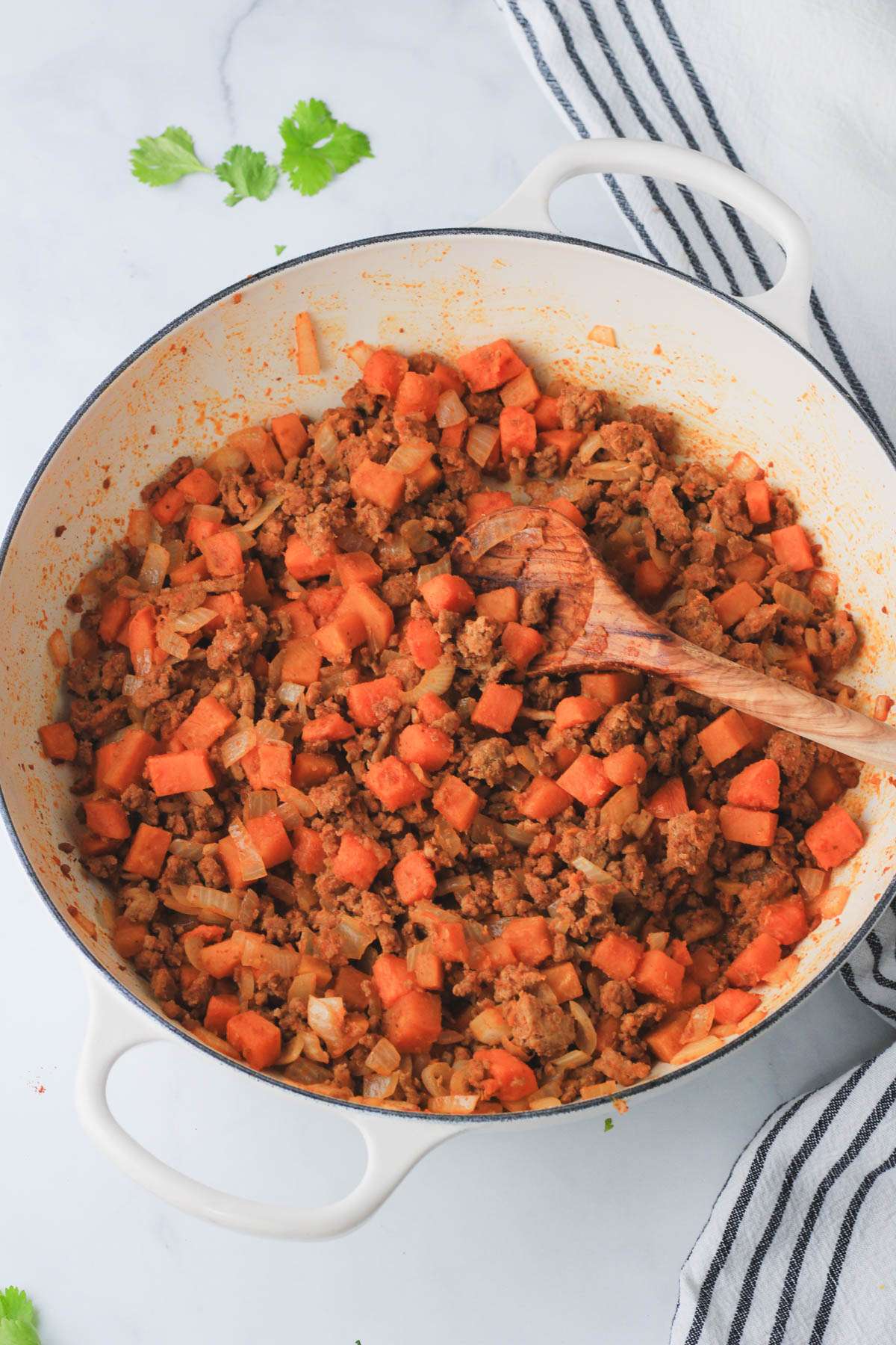 Cooked ground turkey taco meat with sweet potato and a wooden spoon in a white skillet.