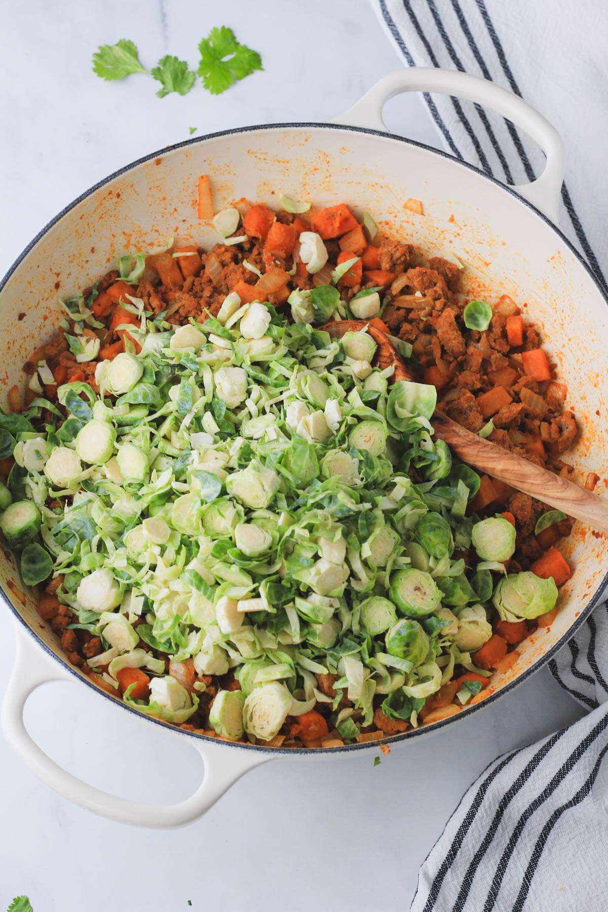 Shaved Brussels sprouts on top of cooked turkey taco meat and sweet potatoes before stirring and cooking together.