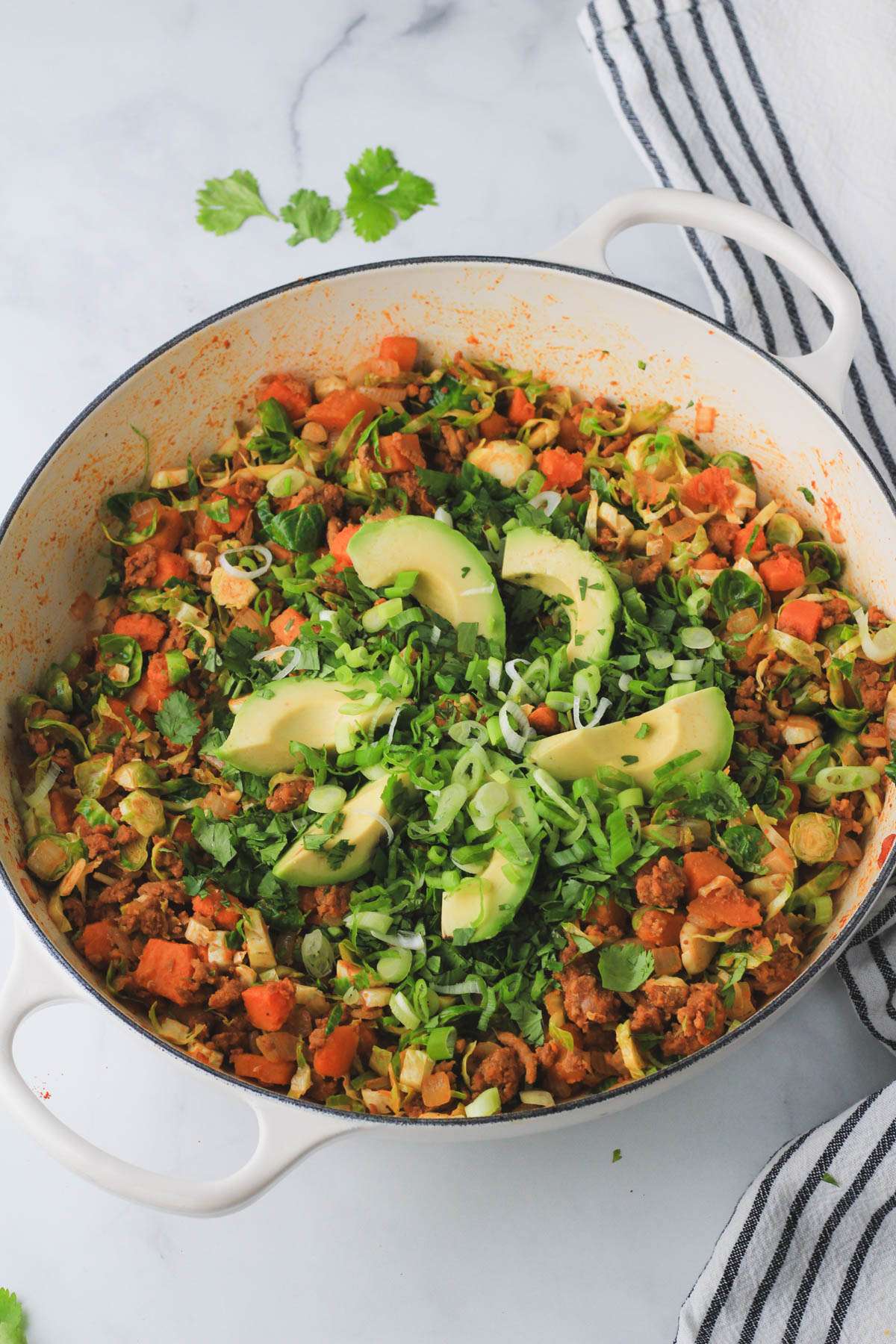A large white skillet with turkey taco meat and sweet potato and topped with fresh avocado, cilantro, and green onion.