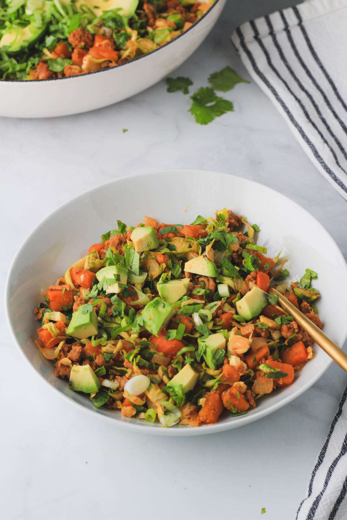 A small white bowl of turkey taco sweet potato skillet with a gold fork on a white counter.