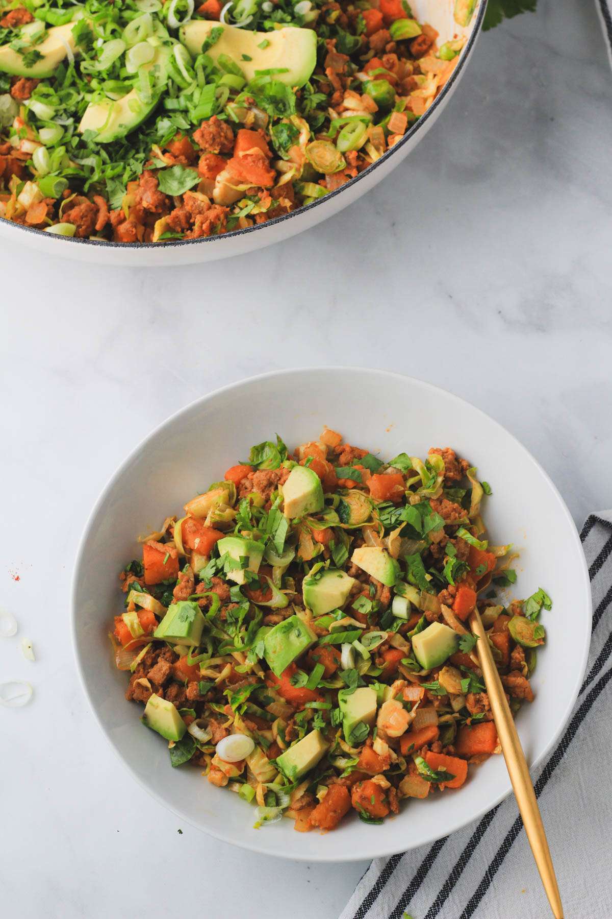 A skillet in the back left and a small bowl in the center with turkey taco sweet potato skillet and a gold fork.
