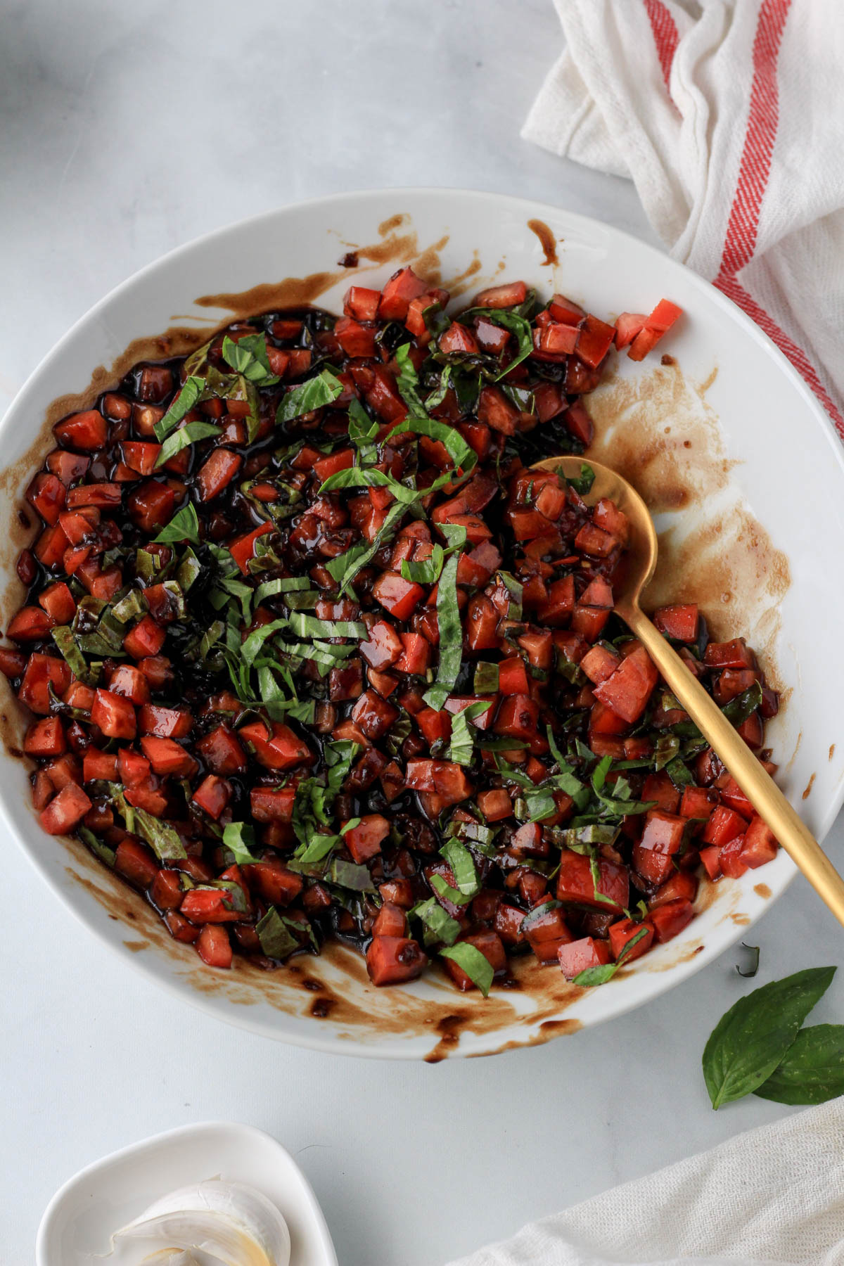A large white bowl with bruschetta topping and a gold spoon after mixing together.