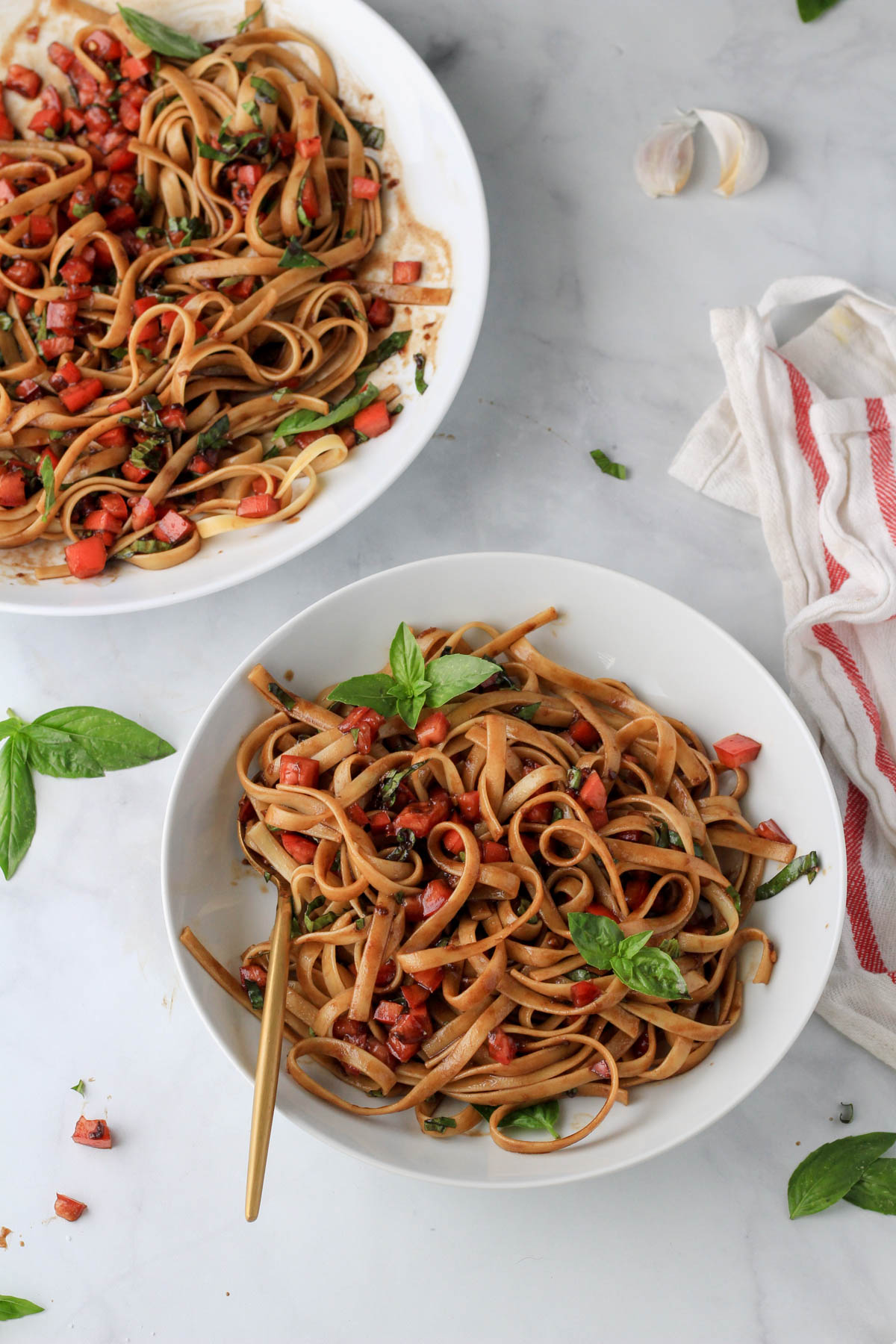 A small white bowl with bruschetta pasta and a larger white bowl of pasta in the back left.