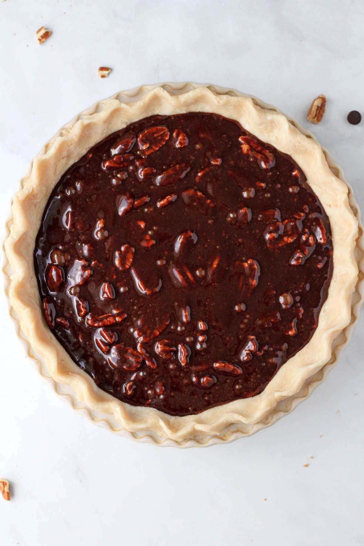 An unbaked pie dough filled with dairy-free chocolate pecan pie before baking.