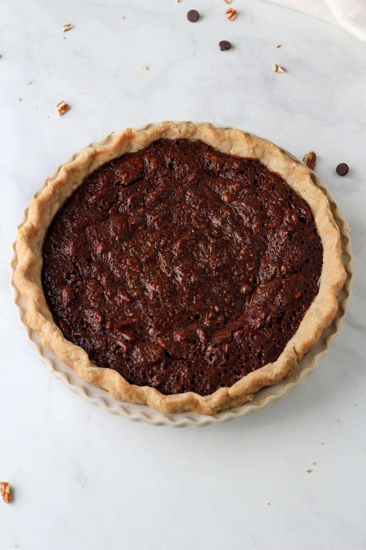 A round pie pan with a chocolate pecan pie after baking.