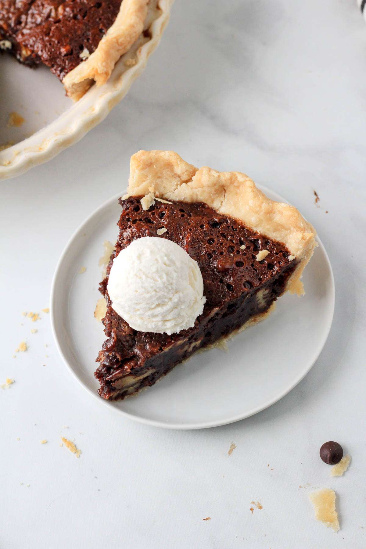 A small white plate with a slice of chocolate pecan pie topped with a scoop of dairy-free vanilla ice cream.