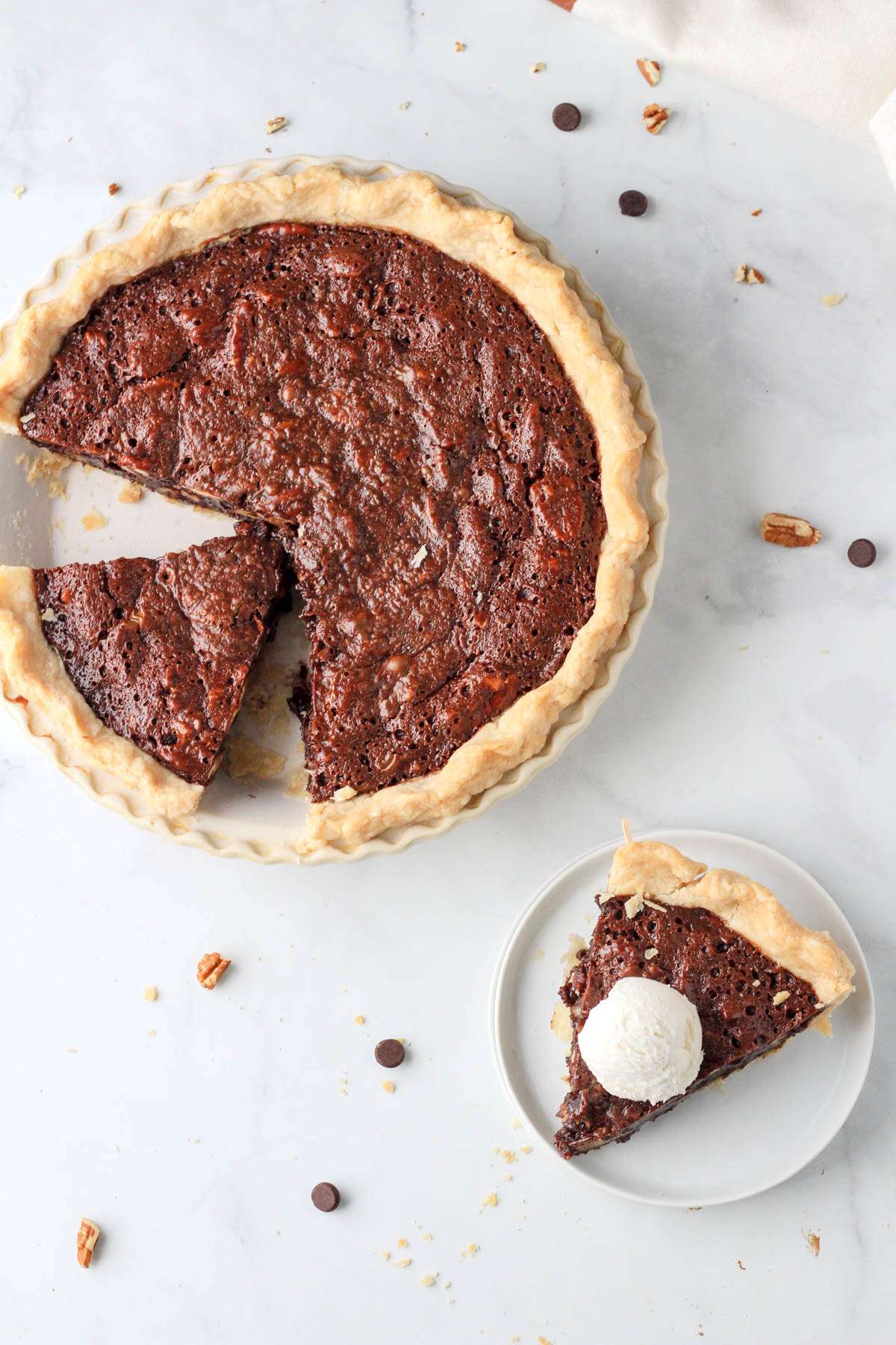 A top down photo of a chocolate pecan pie in the top left with a slice on a white plate in the bottom right.
