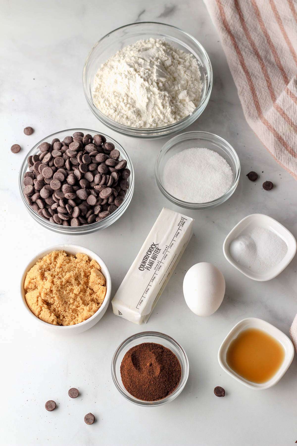 Ingredients for espresso chocolate chip cookies on a white counter with a pink striped towel.