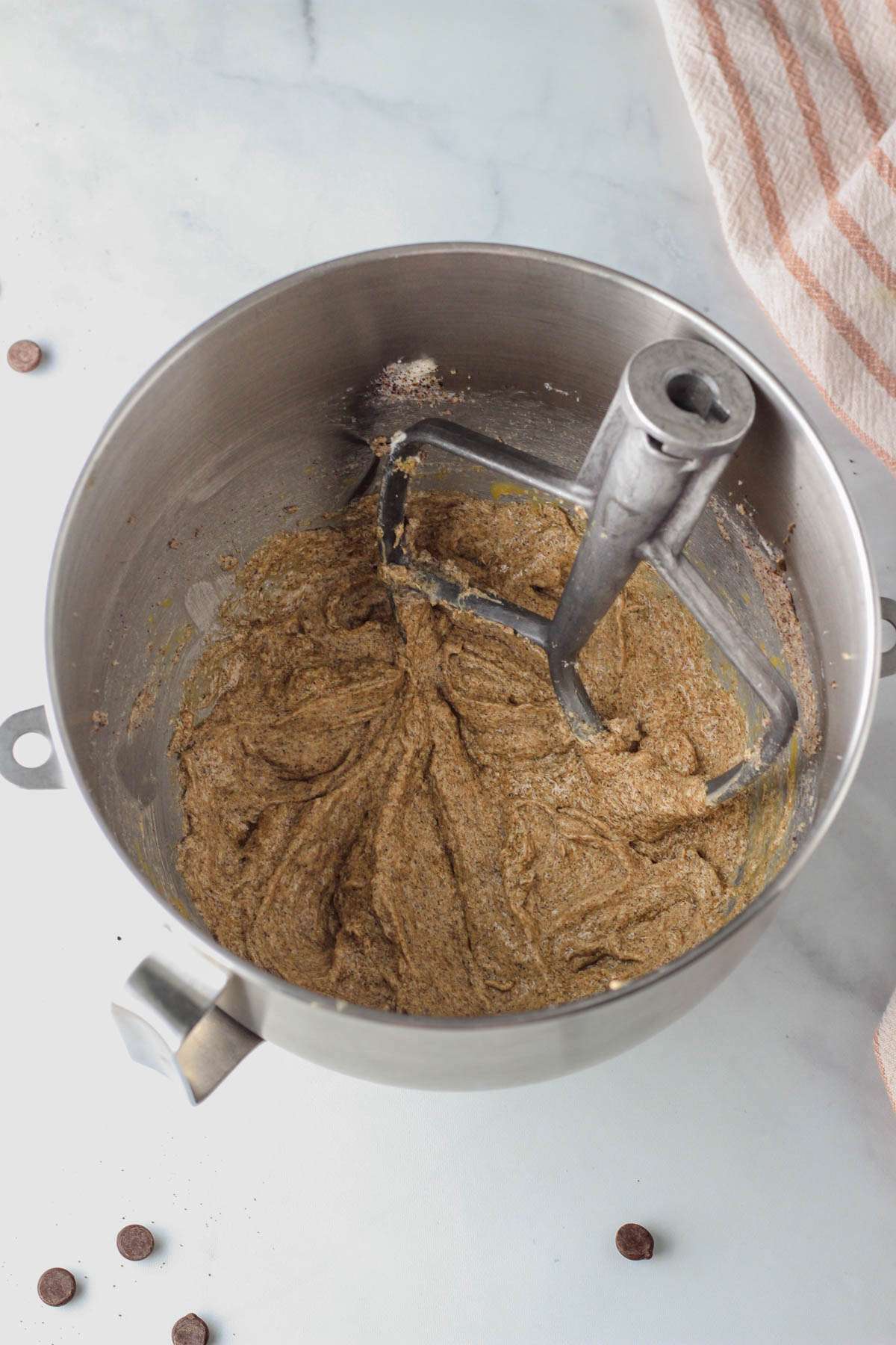 A silver mixing bowl with the paddle attachment and eggs beat into the wet ingredients.