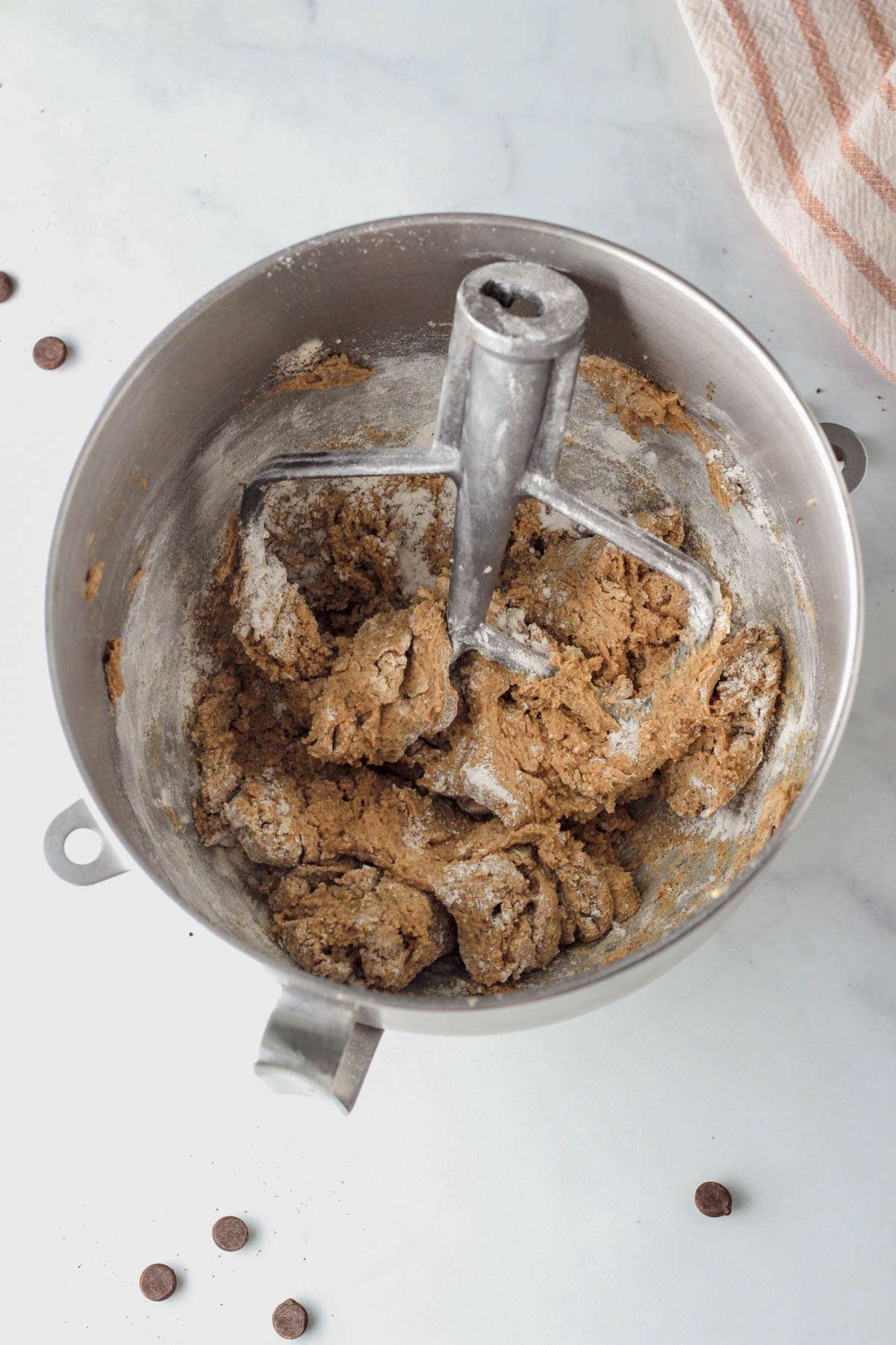 A silver mixing bowl with the paddle attachment and dry ingredients just incorporated into the dough.
