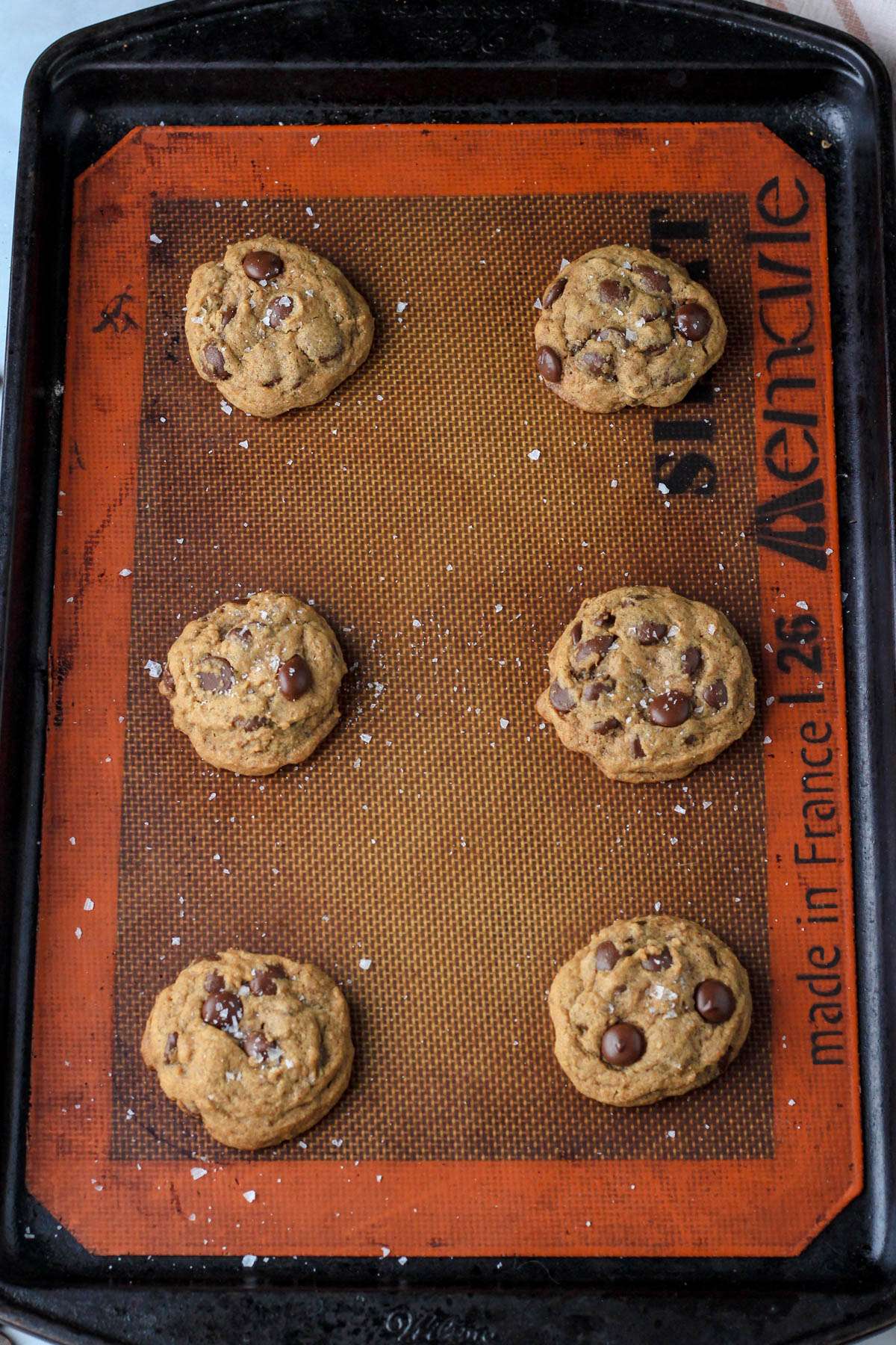 Sea salt topped espresso chocolate chip cookies on a silicone lined baking sheet after baking.