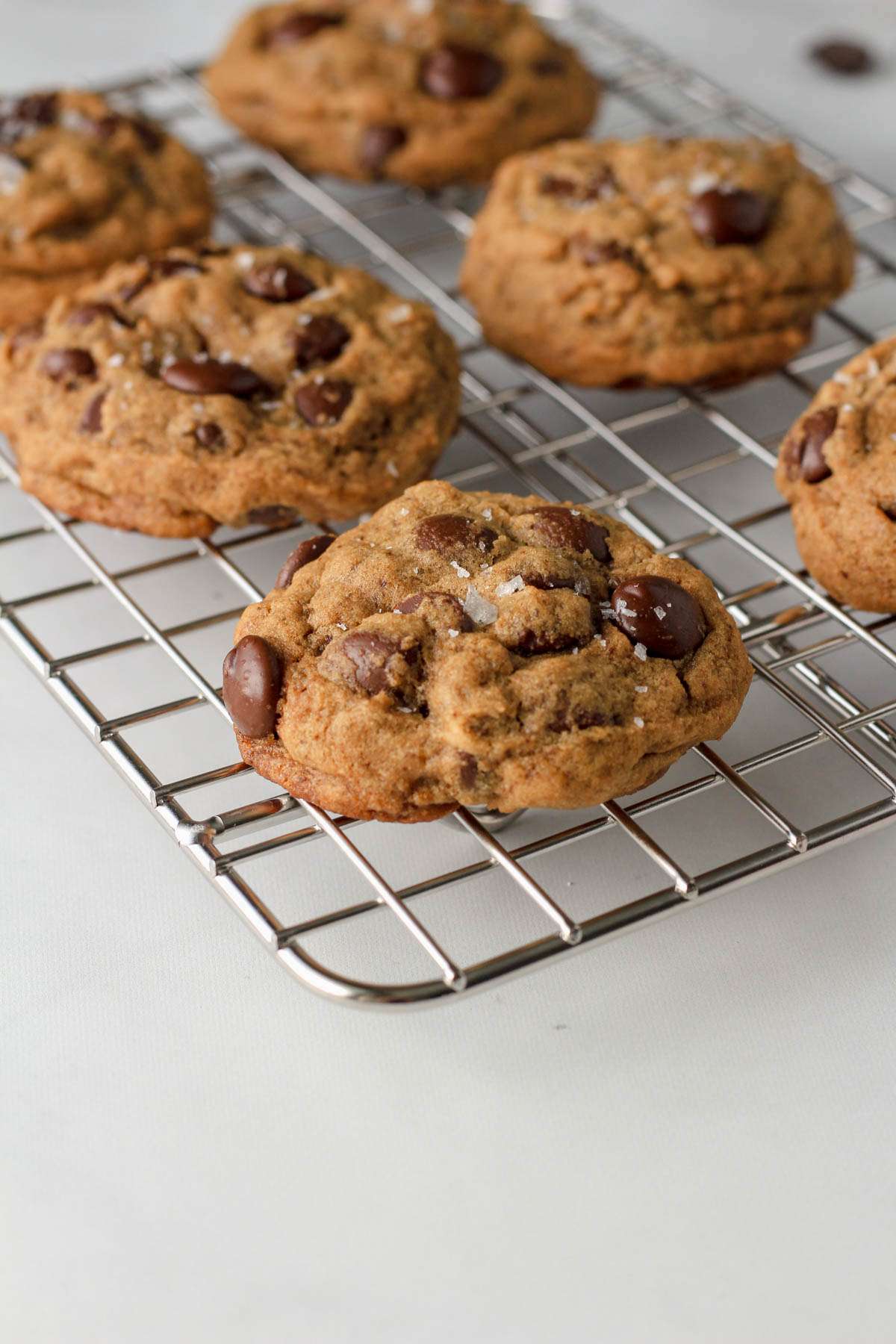 Espresso chocolate chip cookies topped with sea salt on a silver cooling rack from the side angle.
